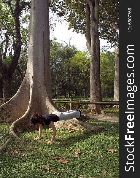 Young, attractive woman is performing a push-up next to a tree. Vertically framed shot. Young, attractive woman is performing a push-up next to a tree. Vertically framed shot