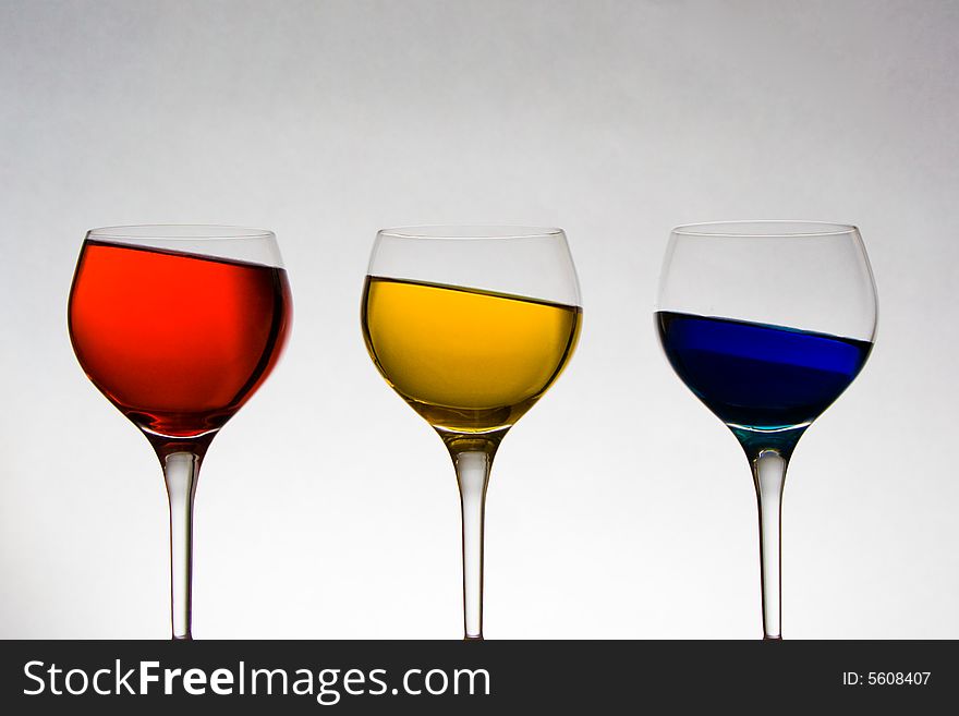 Three wine glasses with red, yellow, and blue liquid at an odd angle. Three wine glasses with red, yellow, and blue liquid at an odd angle