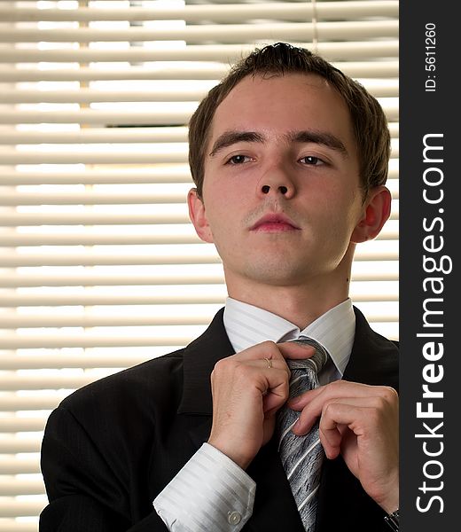 Young businessman ties necktie in office room. Young businessman ties necktie in office room