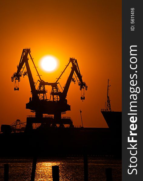 A pair of cargo cranes sit at rest in a industrial shipyard at sunset. A pair of cargo cranes sit at rest in a industrial shipyard at sunset