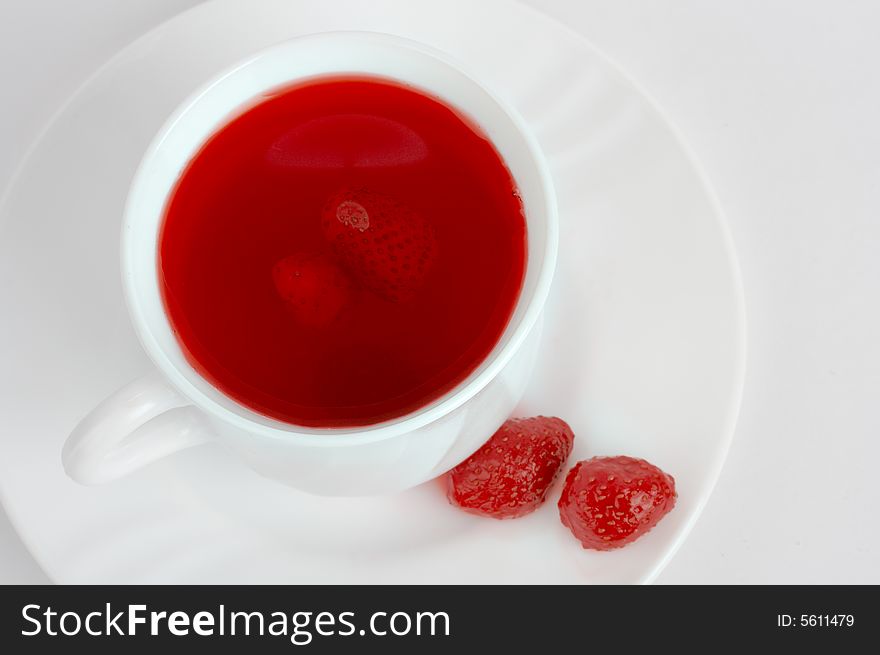 Red strawberry drink in white tea cup with two strawberries on a white plate. White background