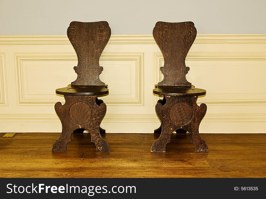 A pair of antique oak chairs in a part panelled classic interior