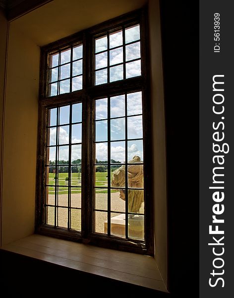 A sunny outlook from a stone mullioned window onto a bright and expansive fromal garden. A sunny outlook from a stone mullioned window onto a bright and expansive fromal garden