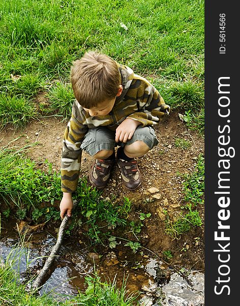 Boy plays in a stream with a stick. Boy plays in a stream with a stick.