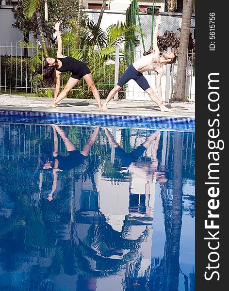 A couple, next to the pool, stretch their sides, together, looking at the sky - vertically framed. A couple, next to the pool, stretch their sides, together, looking at the sky - vertically framed