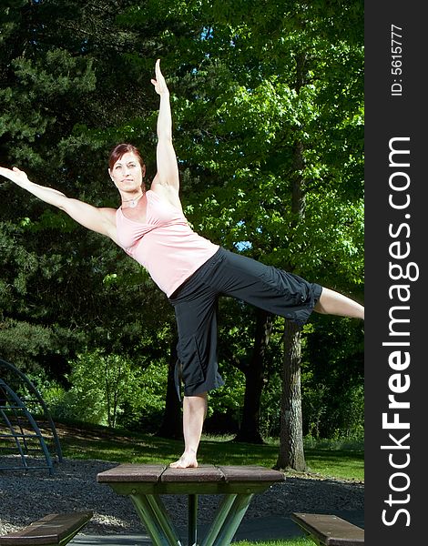 Physically fit woman standing on picnic table in the park. Posed in yoga position, balanced on right foot. Vertically framed shot. Physically fit woman standing on picnic table in the park. Posed in yoga position, balanced on right foot. Vertically framed shot.