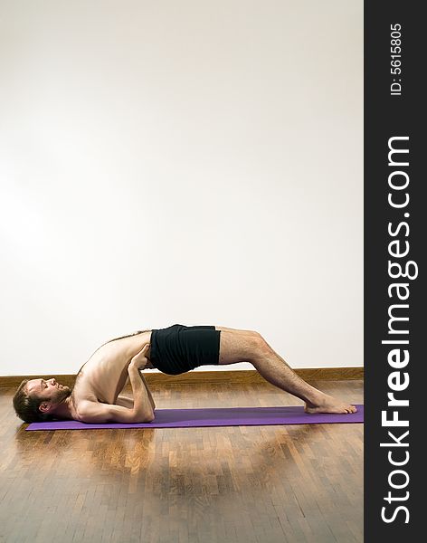 Man performing yoga on mat. Lying on shoulders, feet on ground, arms supporting back. Vertically framed shot. Man performing yoga on mat. Lying on shoulders, feet on ground, arms supporting back. Vertically framed shot.