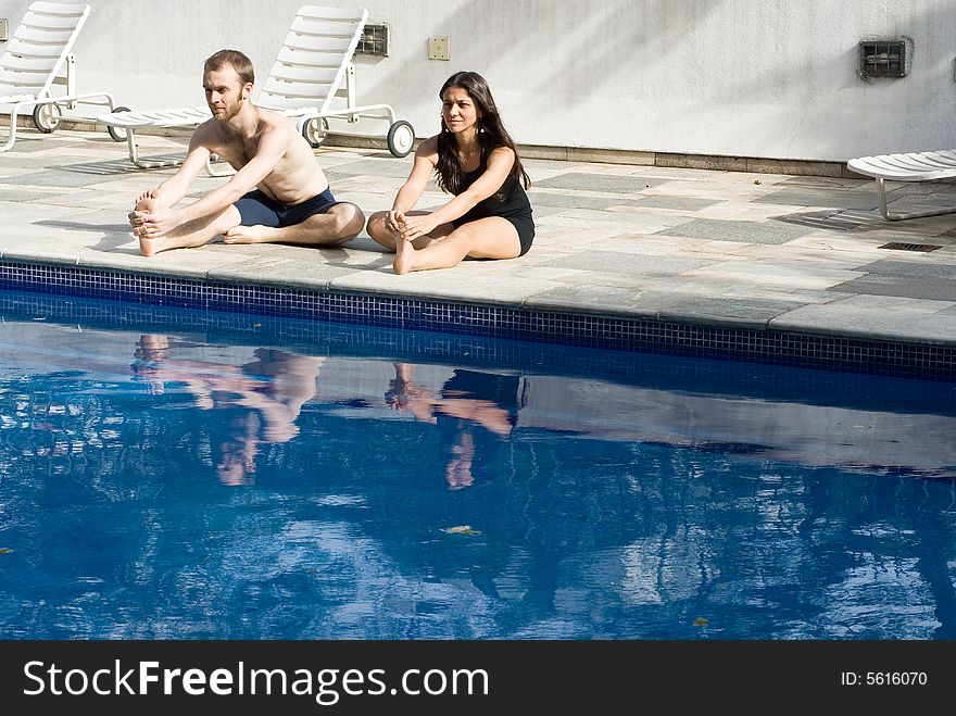A couple stretching their legs by the poolside, smiling and concentrating - horizontally framed. A couple stretching their legs by the poolside, smiling and concentrating - horizontally framed