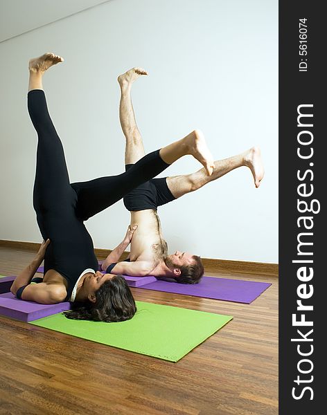 Man and woman performing yoga together on mats. Lying on shoulders, feet in air above head, legs spread. Vertically framed shot. Man and woman performing yoga together on mats. Lying on shoulders, feet in air above head, legs spread. Vertically framed shot.