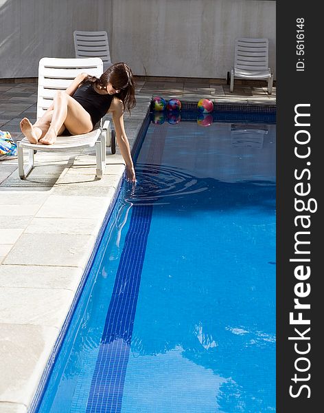 A young, attractive, girl, lies in a poolside chair, dipping her hand in the pool - vertically framed. A young, attractive, girl, lies in a poolside chair, dipping her hand in the pool - vertically framed