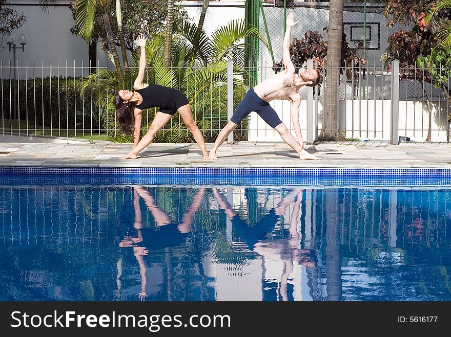 A couple, by the poolside, stretch their sides, together - horizontally framed. A couple, by the poolside, stretch their sides, together - horizontally framed