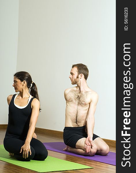 Man and woman performing yoga together on mats. Sitting position, head turned over right shoulder. Vertically framed shot. Man and woman performing yoga together on mats. Sitting position, head turned over right shoulder. Vertically framed shot.