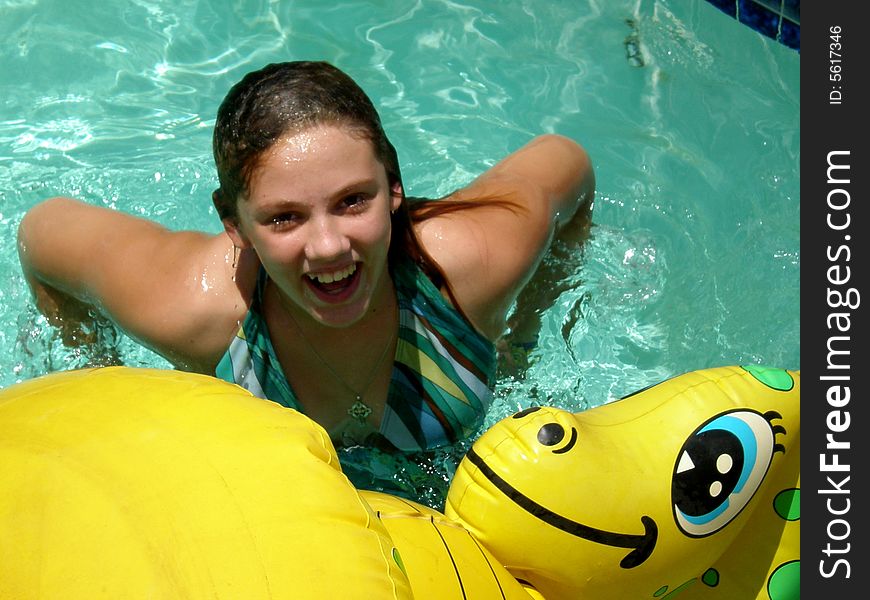 A picture of a cute girl smiling in the swimming pool with a dragon floaty toy. A picture of a cute girl smiling in the swimming pool with a dragon floaty toy.