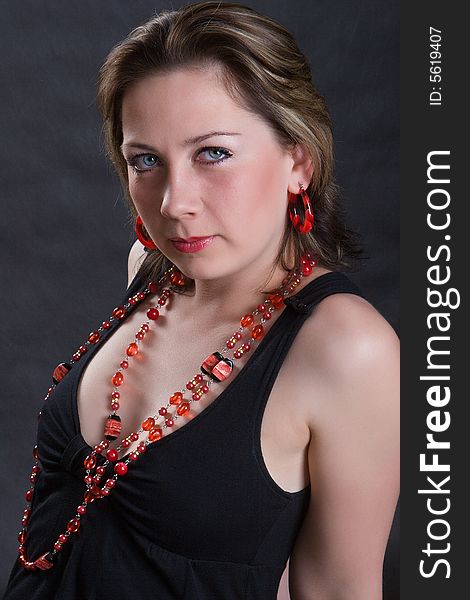 Portrait of the beautiful young girl in a red beads on a dark background. Portrait of the beautiful young girl in a red beads on a dark background