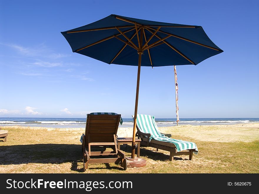 Picture of beach chairs at the beach with beach towel under blue umbrella. Picture of beach chairs at the beach with beach towel under blue umbrella