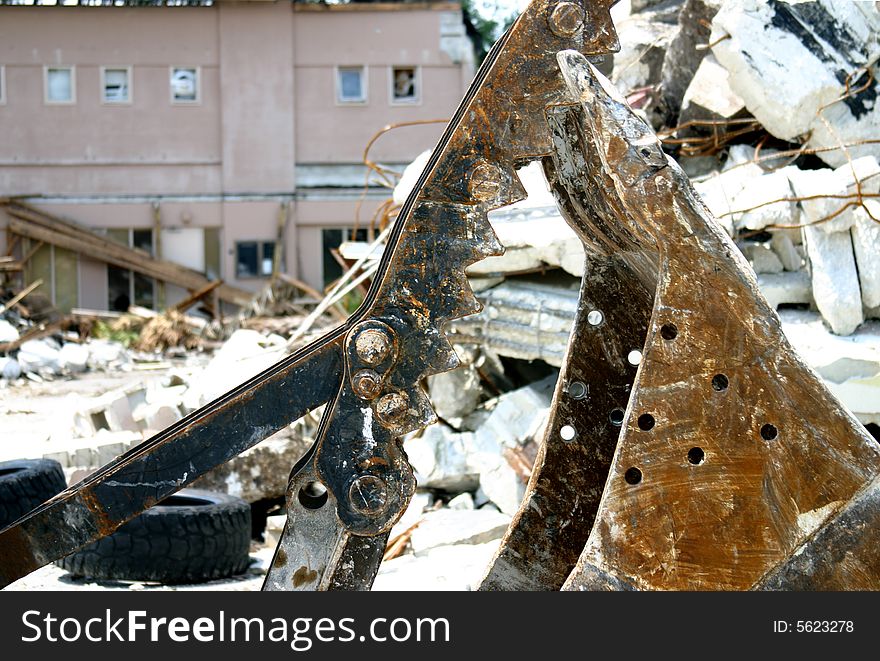 Detail of the business end of a construction shovel with partially torn down building in background. Detail of the business end of a construction shovel with partially torn down building in background