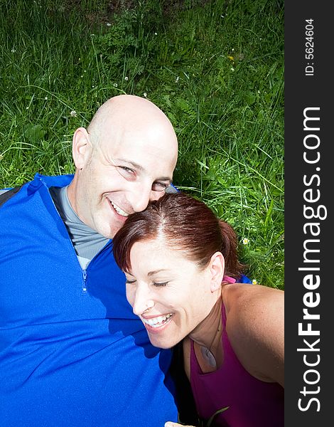 Happy couple sit on the grass in the park. She is leaning on his shoulder. Vertically framed photograph. Happy couple sit on the grass in the park. She is leaning on his shoulder. Vertically framed photograph