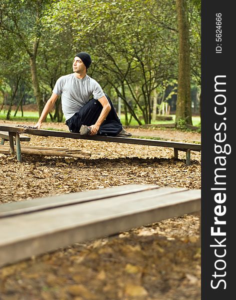 A male, sitting on a park bench, stretching - vertically framed. A male, sitting on a park bench, stretching - vertically framed