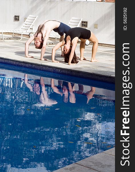 A couple, by the poolside, go into a bridge position to stretch - vertically framed. A couple, by the poolside, go into a bridge position to stretch - vertically framed