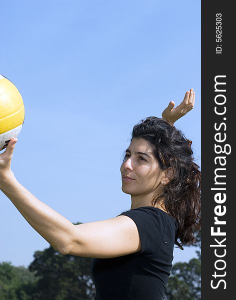 A woman is standing in a park.  She is looking away from the camera.  She is about to spike a volleyball.  Vertically  framed photo. A woman is standing in a park.  She is looking away from the camera.  She is about to spike a volleyball.  Vertically  framed photo.