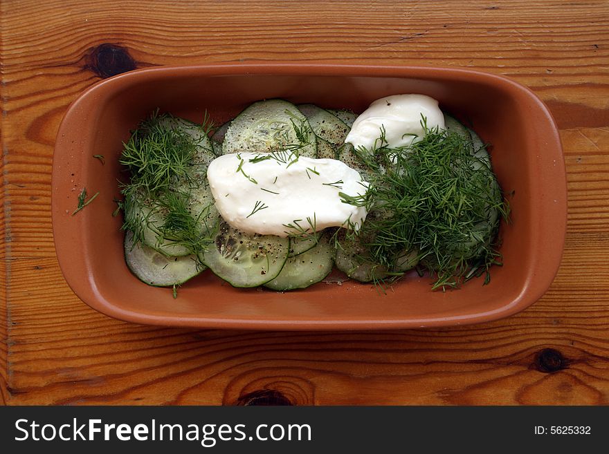 Cucumber salad with sour cream in brown ceramic cup