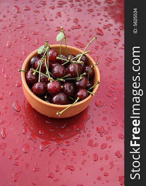 Cherries, with drops of water, in a brown ceramic cup on a red background