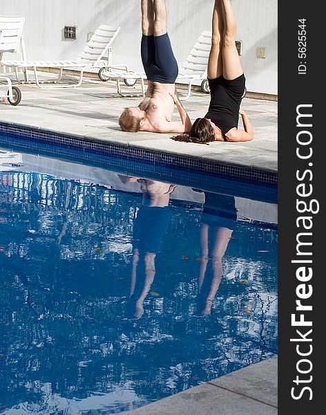A couple, by the pool, stretch with each other, doing candlestick - vertically framed. A couple, by the pool, stretch with each other, doing candlestick - vertically framed