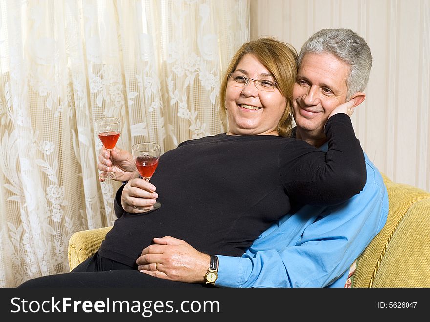 A couple sitting in a chair drinking wine. The woman is on his lap and has her hand on his face. They are smiling. Horizontally framed shot. A couple sitting in a chair drinking wine. The woman is on his lap and has her hand on his face. They are smiling. Horizontally framed shot.