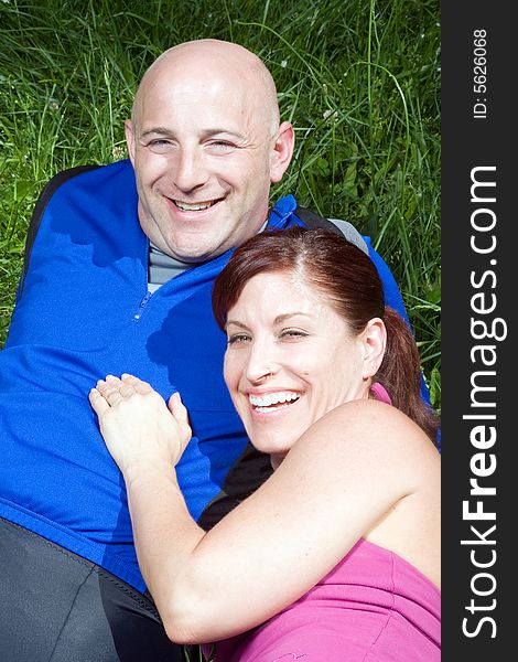 Happy couple sitting on the grass laughing. Vertically framed photograph. Happy couple sitting on the grass laughing. Vertically framed photograph