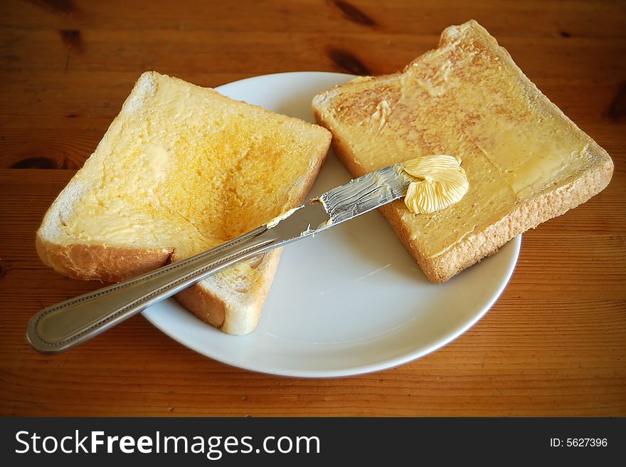 Two pieces of bread with butter and a knife in a wooden table. Two pieces of bread with butter and a knife in a wooden table