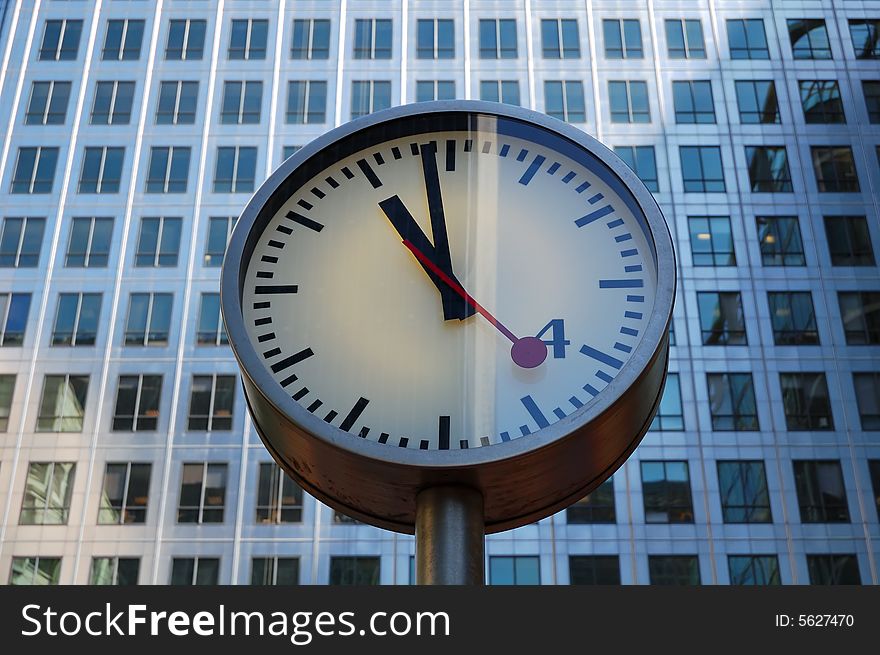 A clock at 11 am with many windows from an office building in the backgroundn. A clock at 11 am with many windows from an office building in the backgroundn