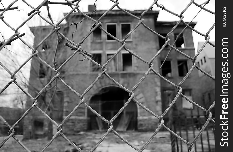 Black and white image of abandoned building behind a fence