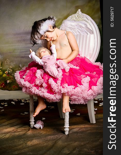 Cute girl wearing angel wings and a pettiskirt is playing with her baby doll. Cute girl wearing angel wings and a pettiskirt is playing with her baby doll