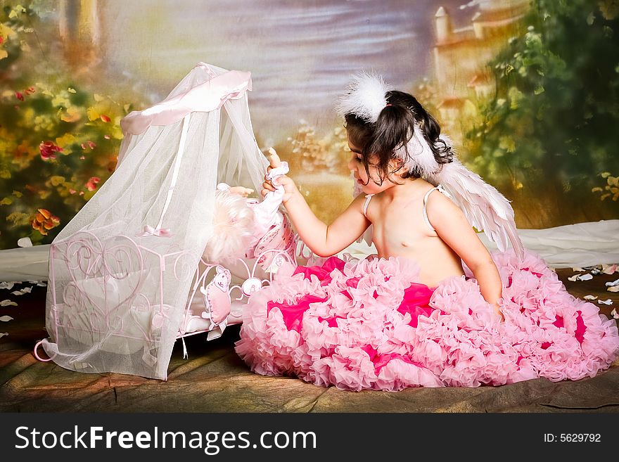 Cute girl wearing angel wings and a pettiskirt is playing with her baby doll. Cute girl wearing angel wings and a pettiskirt is playing with her baby doll
