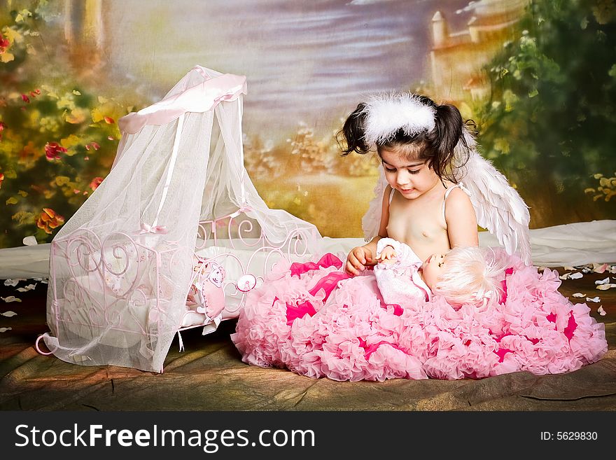 Cute girl wearing angel wings and a pettiskirt is playing with her baby doll. Cute girl wearing angel wings and a pettiskirt is playing with her baby doll