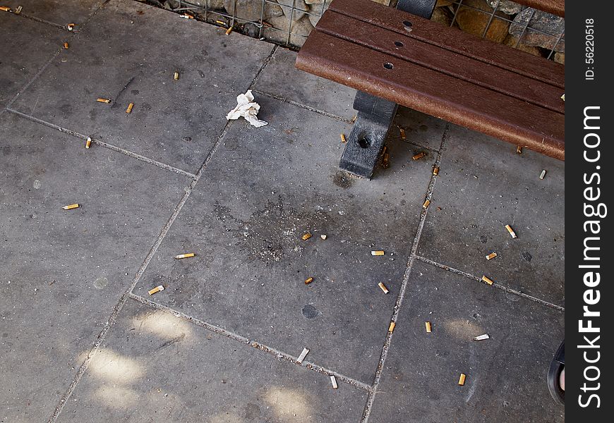 Dirt, litter and cigarette butts next to a city street public bench