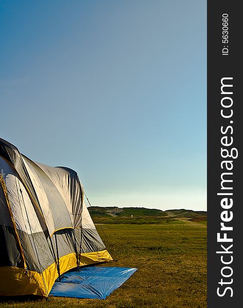 A yellow and gray tent setup on a camp field and with a beach path at a distance. A yellow and gray tent setup on a camp field and with a beach path at a distance.