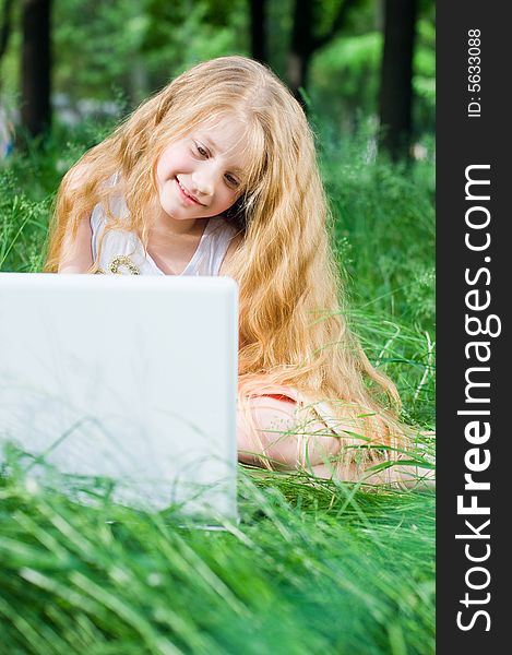 Serious looking little girl with laptop in green grass