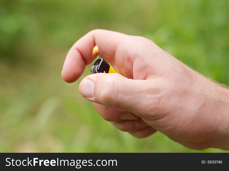 Hand holding yellow lighter with flame, outdoors. Hand holding yellow lighter with flame, outdoors