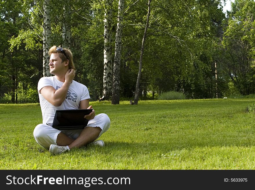 Casual man works on laptop on the grass