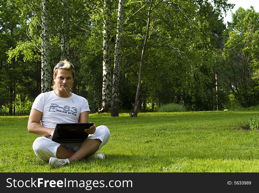 Casual man works on laptop on the grass