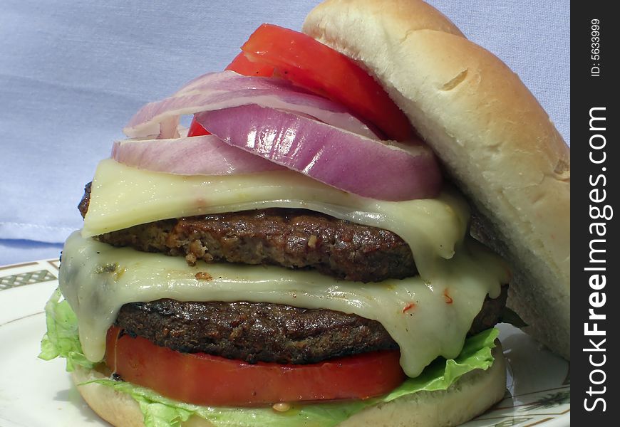 A serving of a thick, juicy and nutritious double hamburger is loaded with vegetables and melted cheese. A serving of a thick, juicy and nutritious double hamburger is loaded with vegetables and melted cheese.