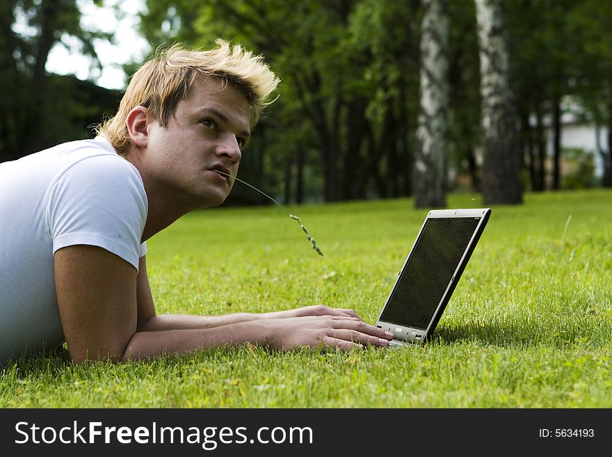 Casual man works on laptop on the grass