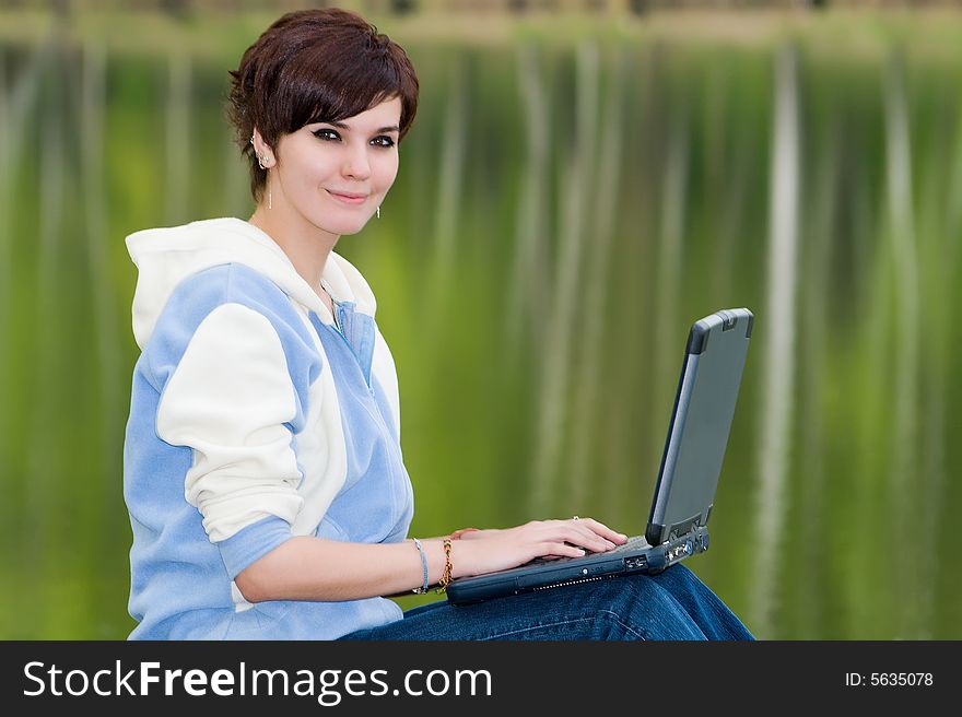 Attractive girl with a portable computer sits on coast of lake