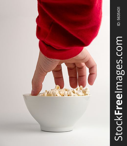 A hand trying to reach some popcorns from a bowl.