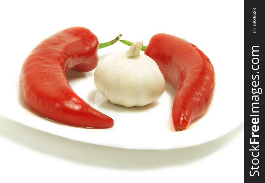 Two fresh chili peppers and a bulb of garlic on a white plate and isolated on white background. Two fresh chili peppers and a bulb of garlic on a white plate and isolated on white background