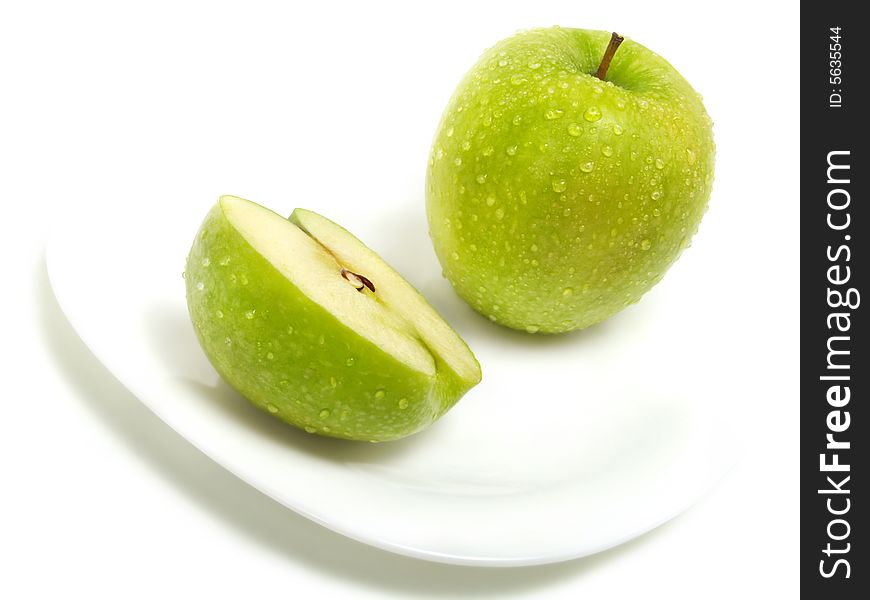 A half and a whole fresh ripe green apple with water drops on white plate and isolated on white background. A half and a whole fresh ripe green apple with water drops on white plate and isolated on white background