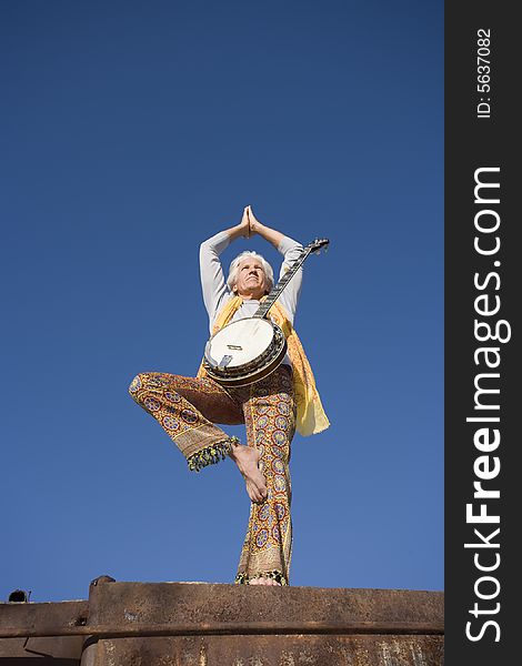 Banjo player standing in a Yoga pose against the blue sky. Banjo player standing in a Yoga pose against the blue sky