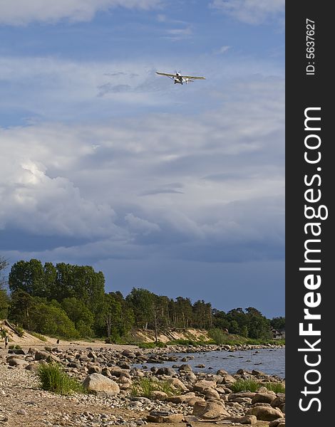 Plane, flying in the blue, cloudy sky above the green forest and stone sea coast. Plane, flying in the blue, cloudy sky above the green forest and stone sea coast