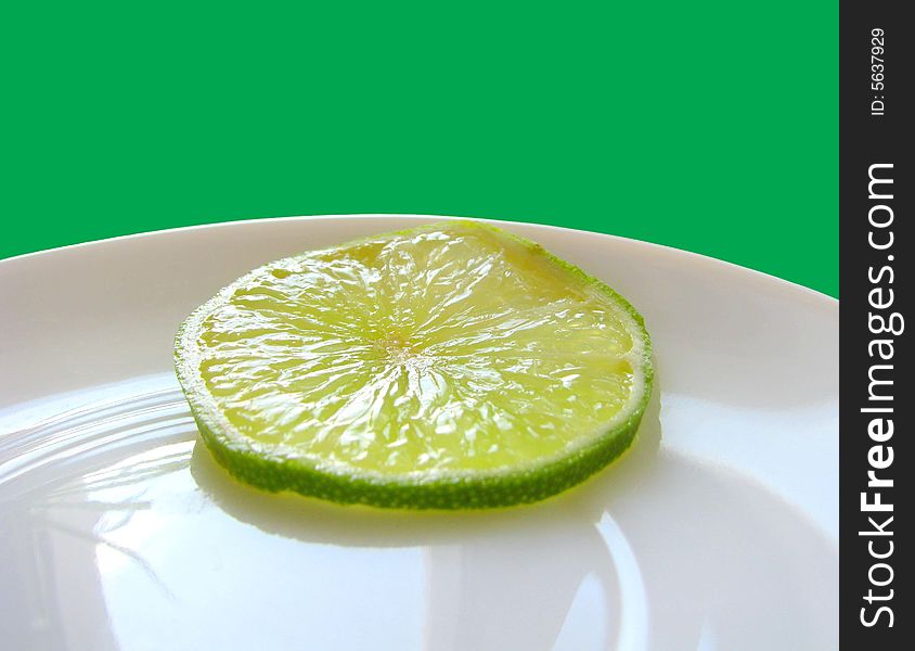 One piese of lime on white plate.Green backgrownd. One piese of lime on white plate.Green backgrownd